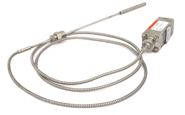 Compact temperature switch with a stainless steel probe and flexible conduit. Industrial temperature control component for monitoring and regulation.