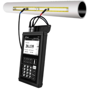 Portable flow meter measuring flow rate in a pipe. The ultrasonic device displays a reading of 20.135. Cables connect the meter to sensors on the pipe.